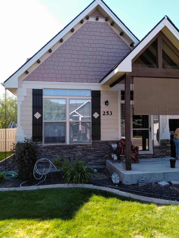 House exterior with stone facade, light siding, and mauve shingles. Black shutters, front door, and a covered porch.