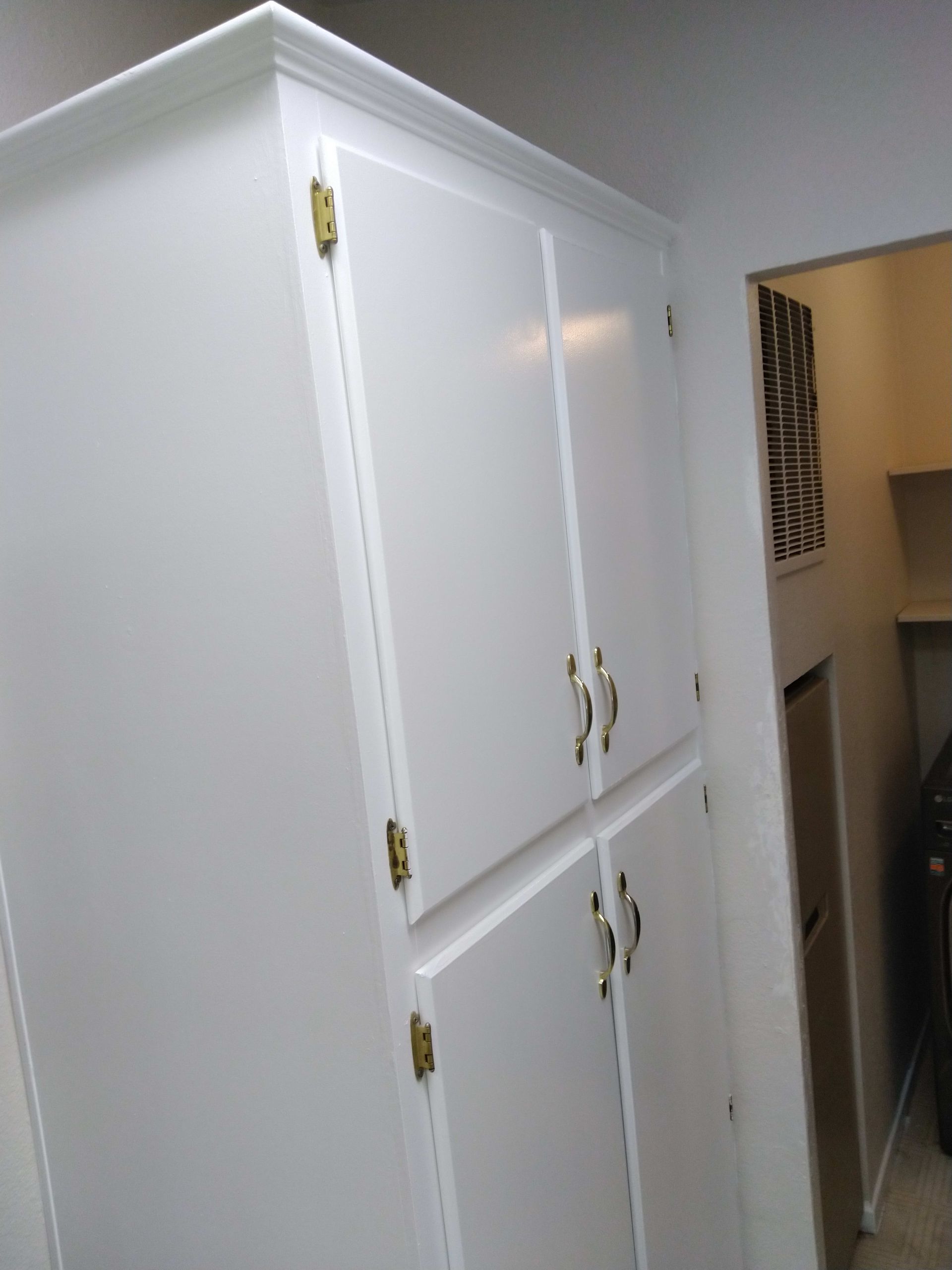 White storage cabinets with gold hardware, in a narrow hallway.