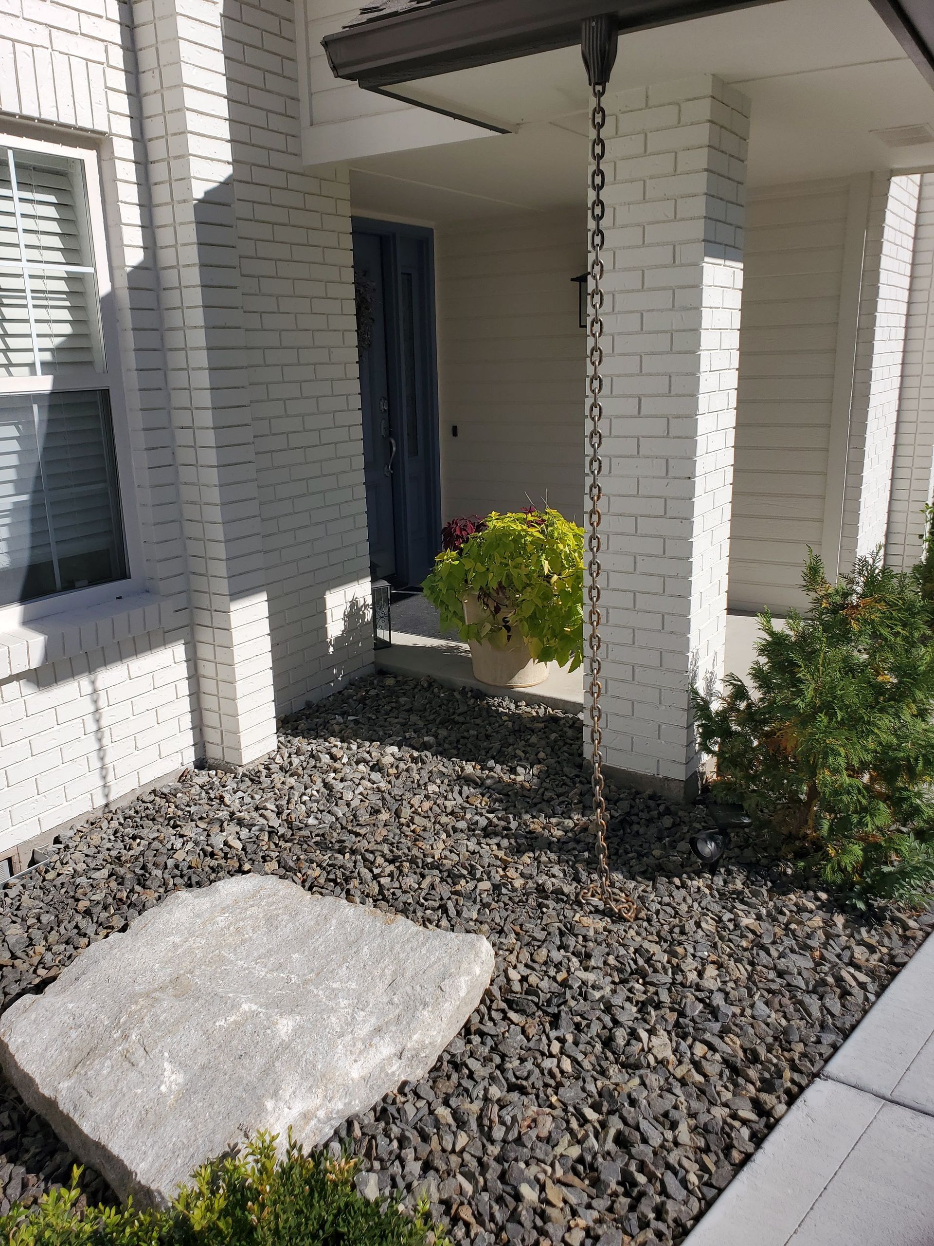 Brick home entrance with rain chain, stone ground cover, and large rock.