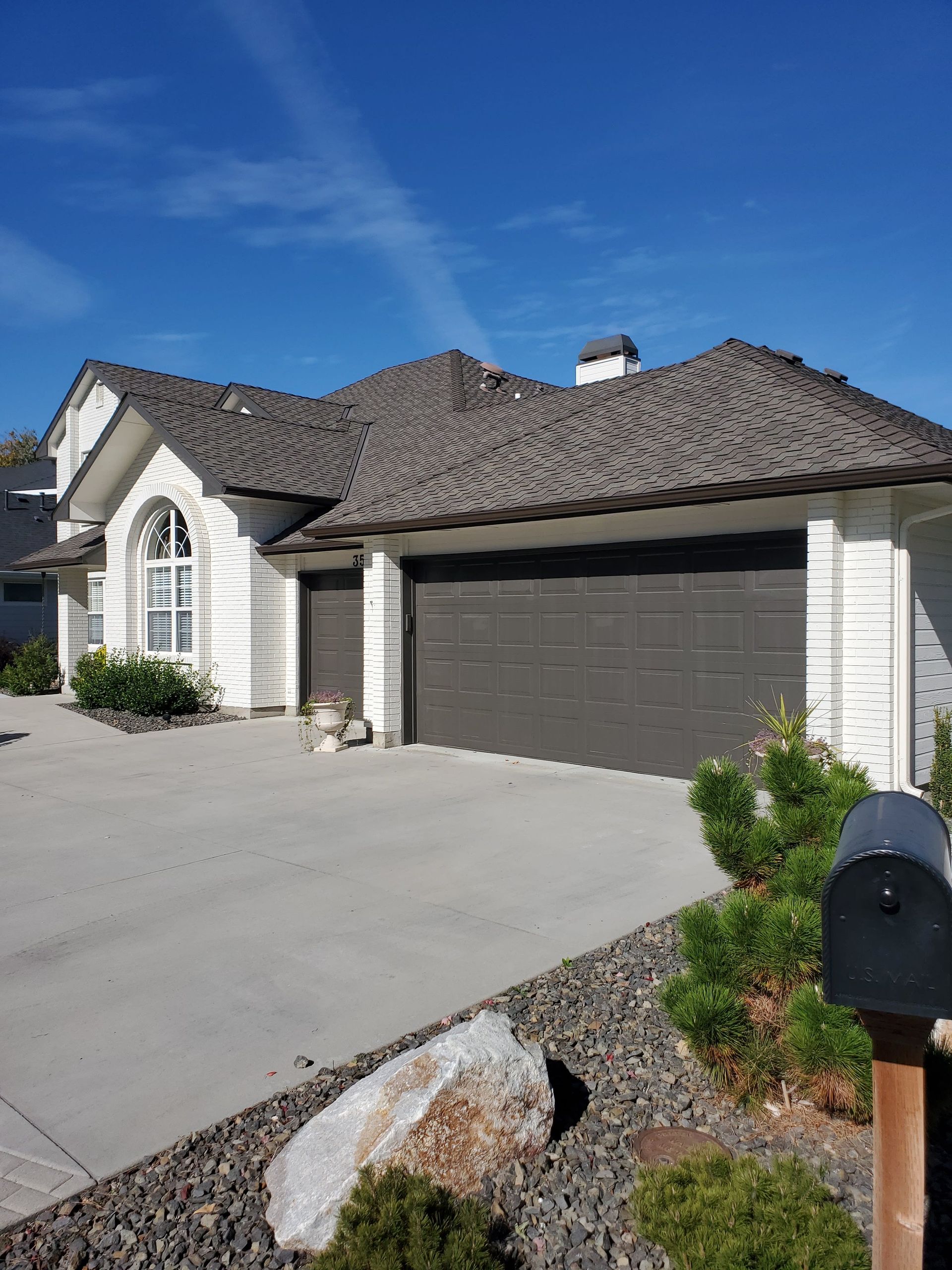 White house with dark garage doors, brown roof, and blue sky.