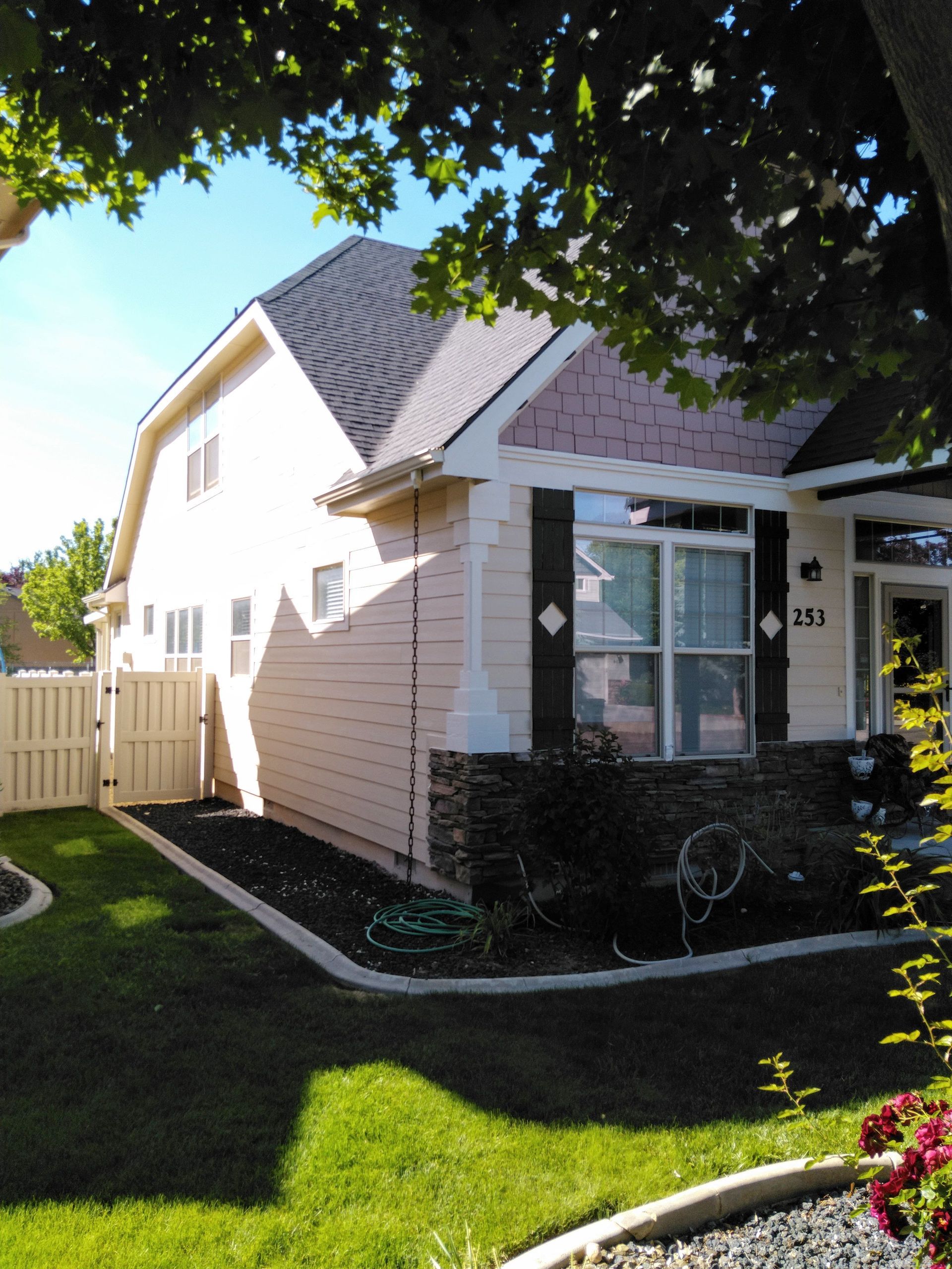 Two-story house with a pink and beige exterior, white fence, and green lawn under a sunny sky.