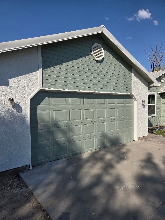 Garage with green door and teal siding under a white roof. Gray concrete driveway.