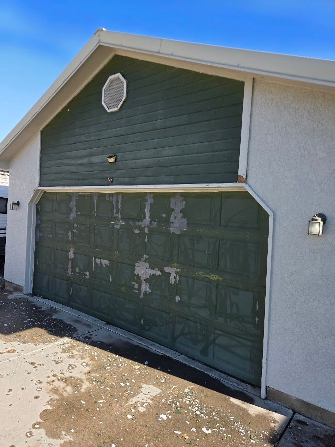 Green garage door with peeling paint and matching upper facade. Light fixture to the right.