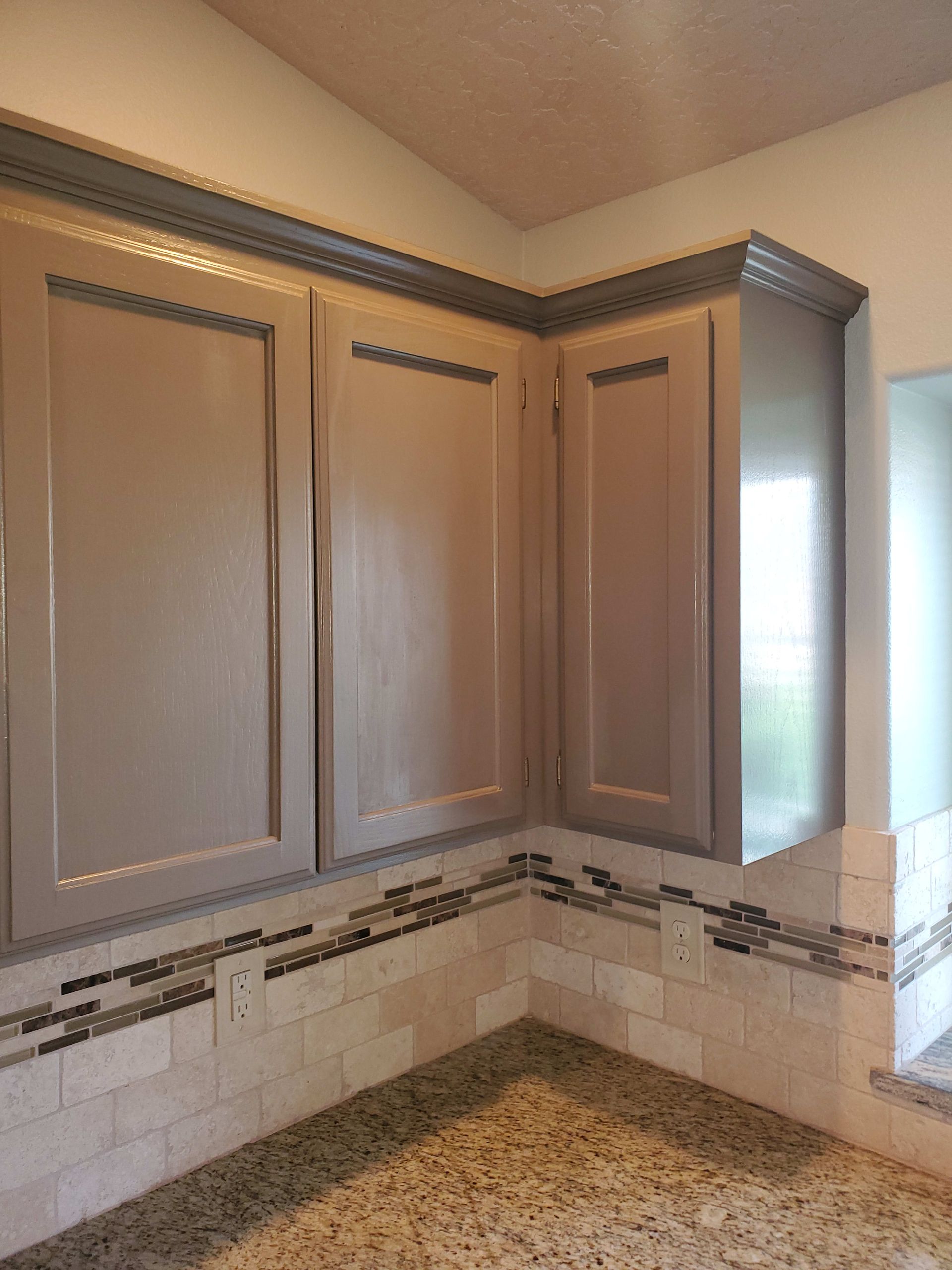 Beige kitchen cabinets with gray trim, granite countertop, and tiled backsplash.