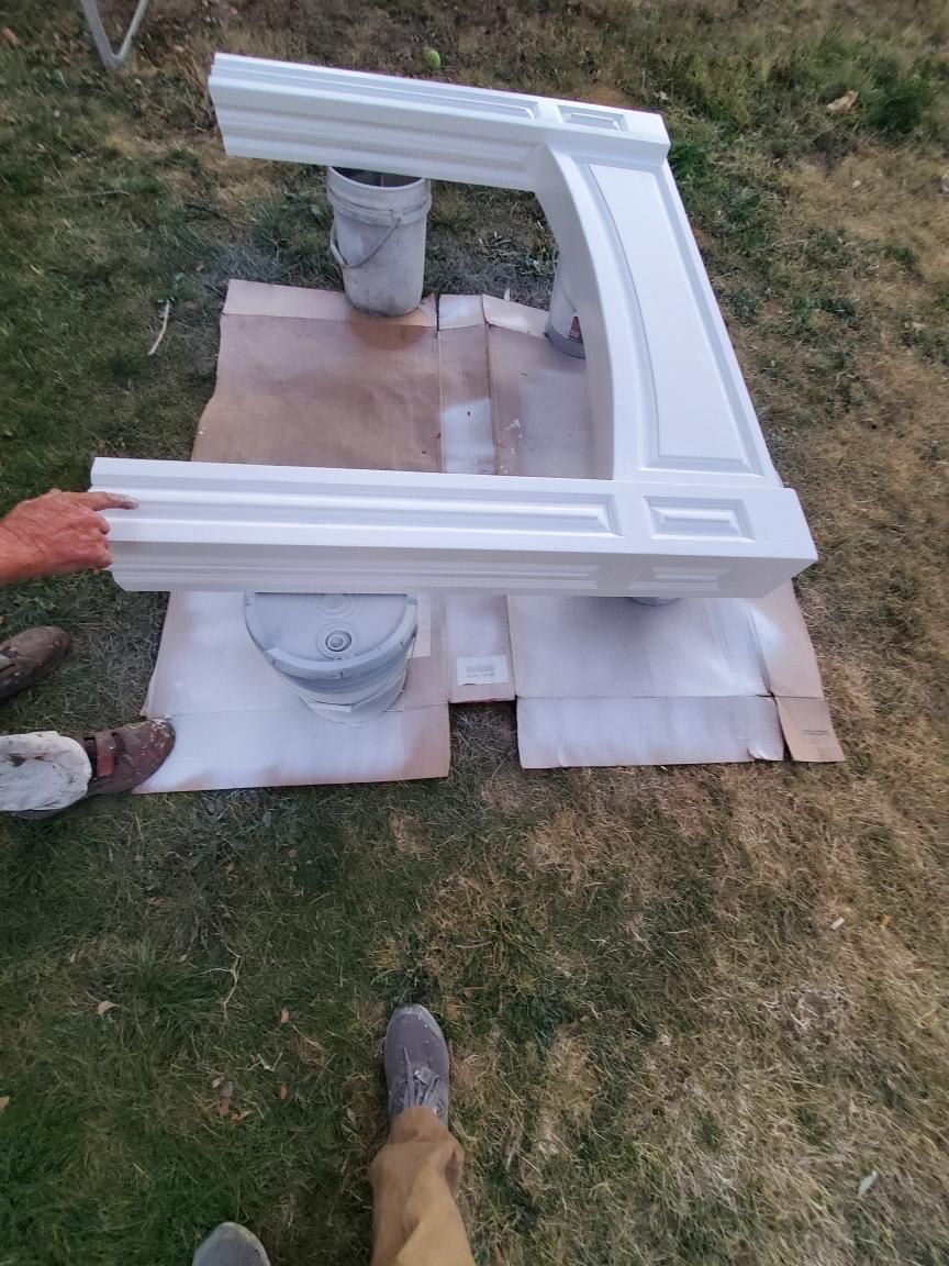 Person spray painting a white fireplace mantel outdoors on cardboard.