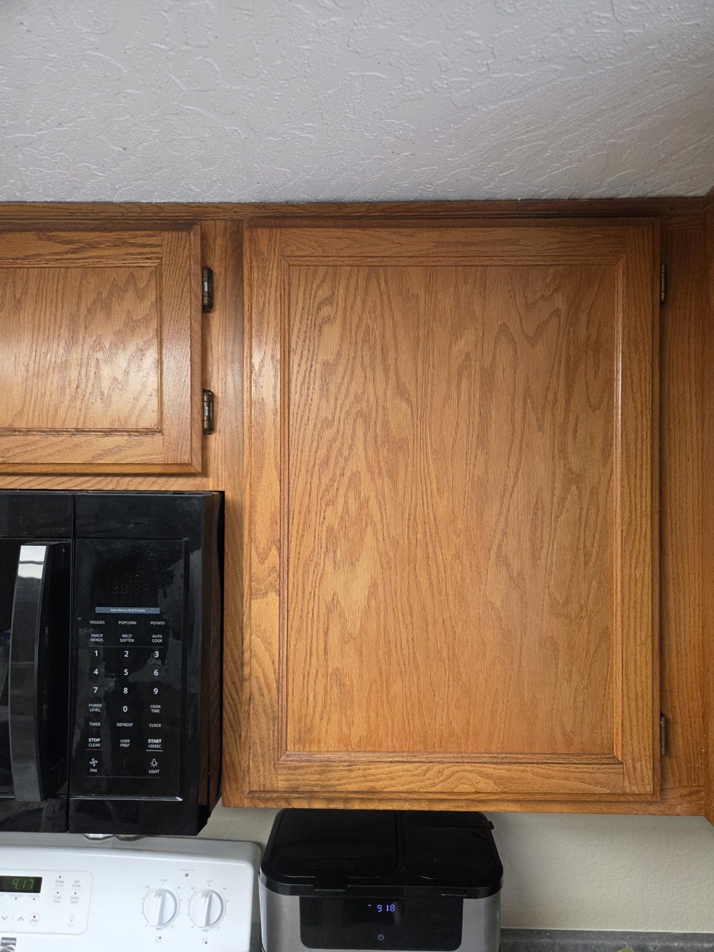 Oak kitchen cabinet, closed, with microwave and appliance below.