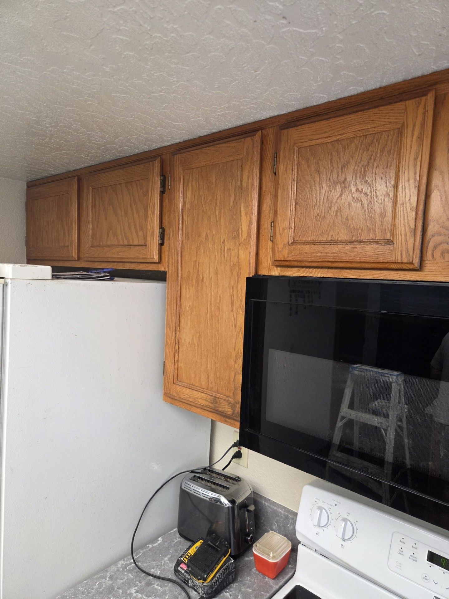 Kitchen cabinets above refrigerator, oven, and stove. Wooden cabinets in varying shades of brown.