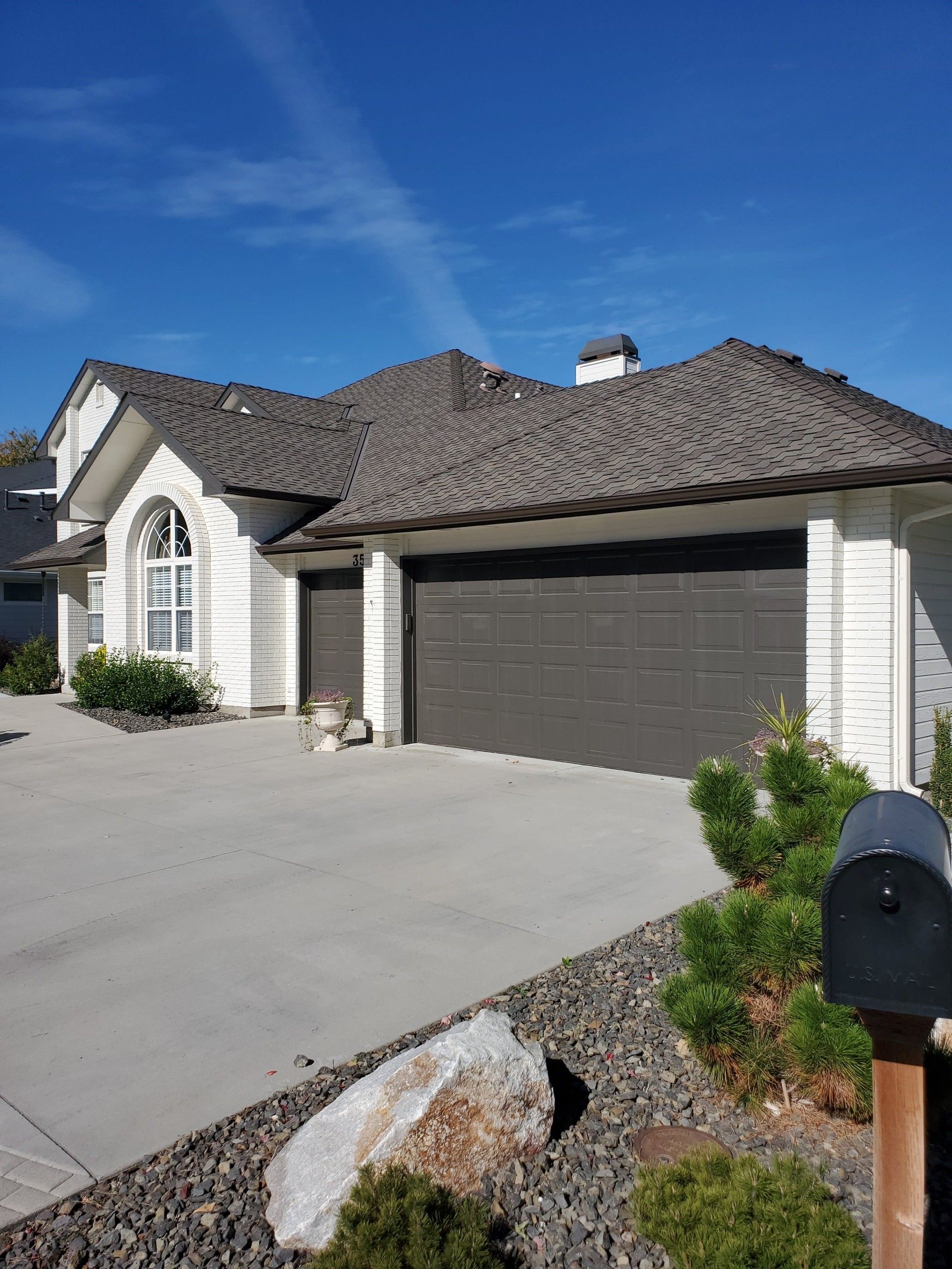 House with brown roof and garage doors, white exterior, driveway, and blue sky.