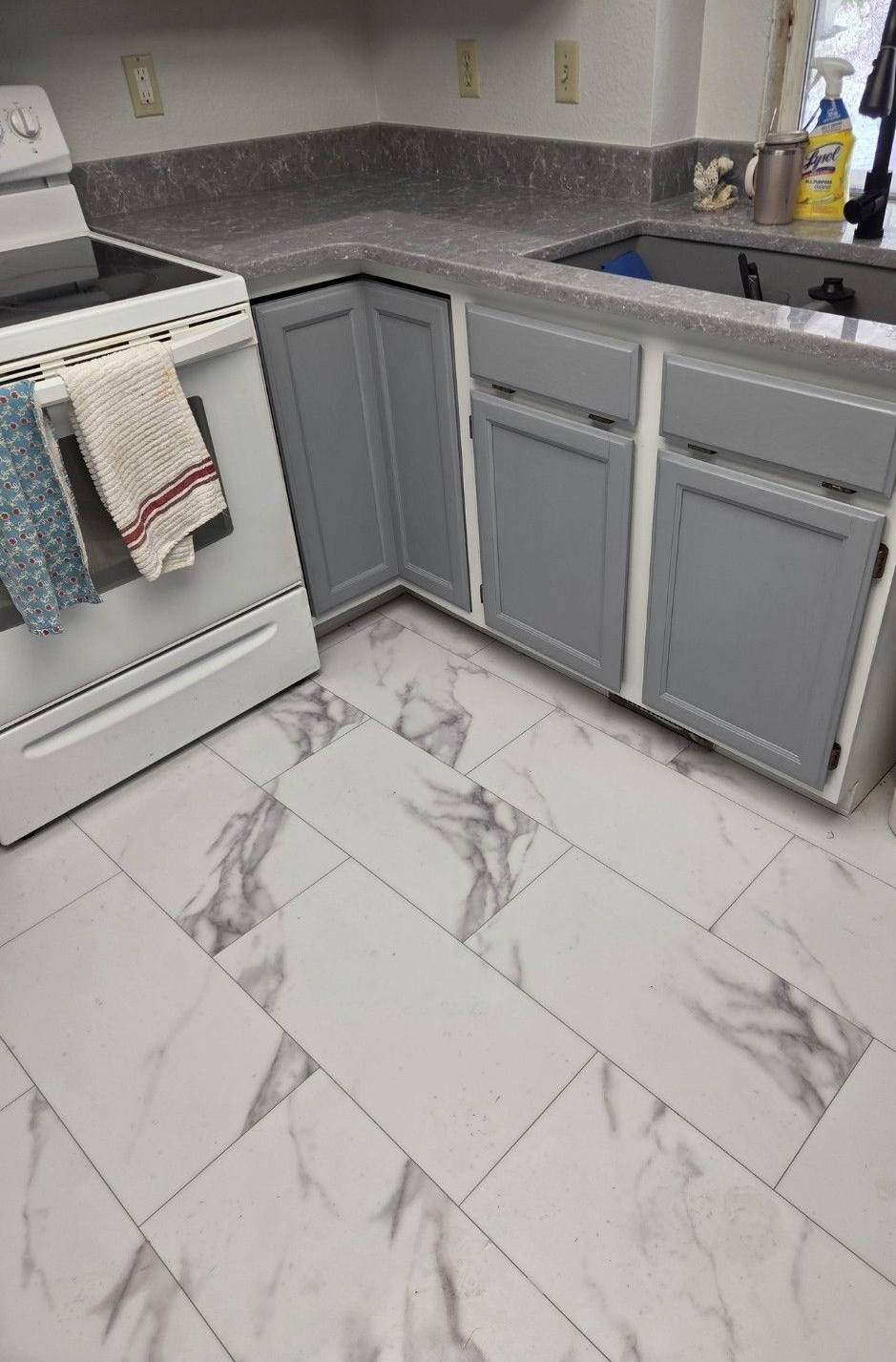 Kitchen with gray cabinets and marble-patterned floor tiles. A white stove is on the left.