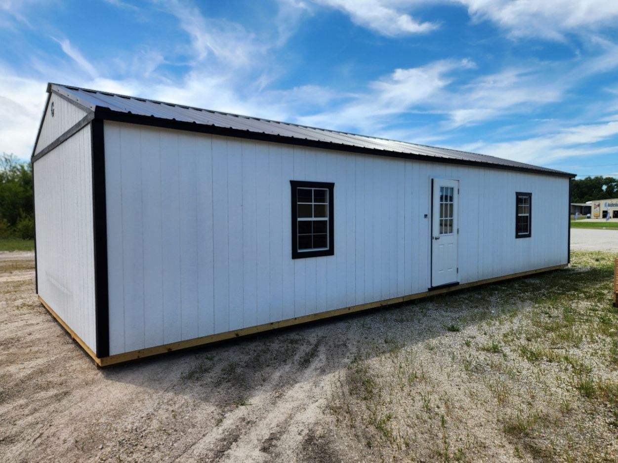 A long white building with black trim is sitting in the middle of a dirt field.