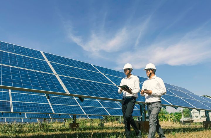 Two men are walking in front of a solar panel field.