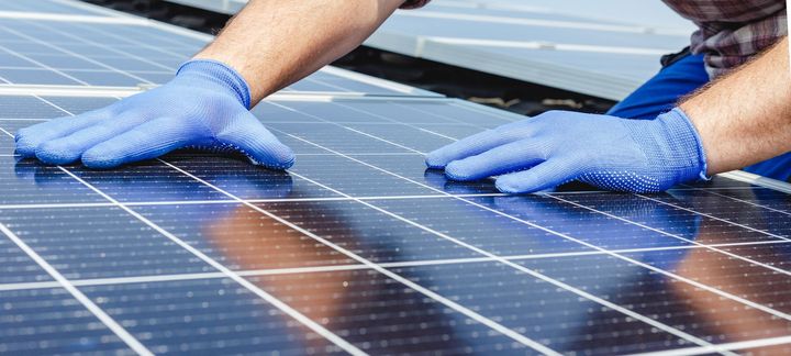 A person wearing blue gloves is working on a solar panel.