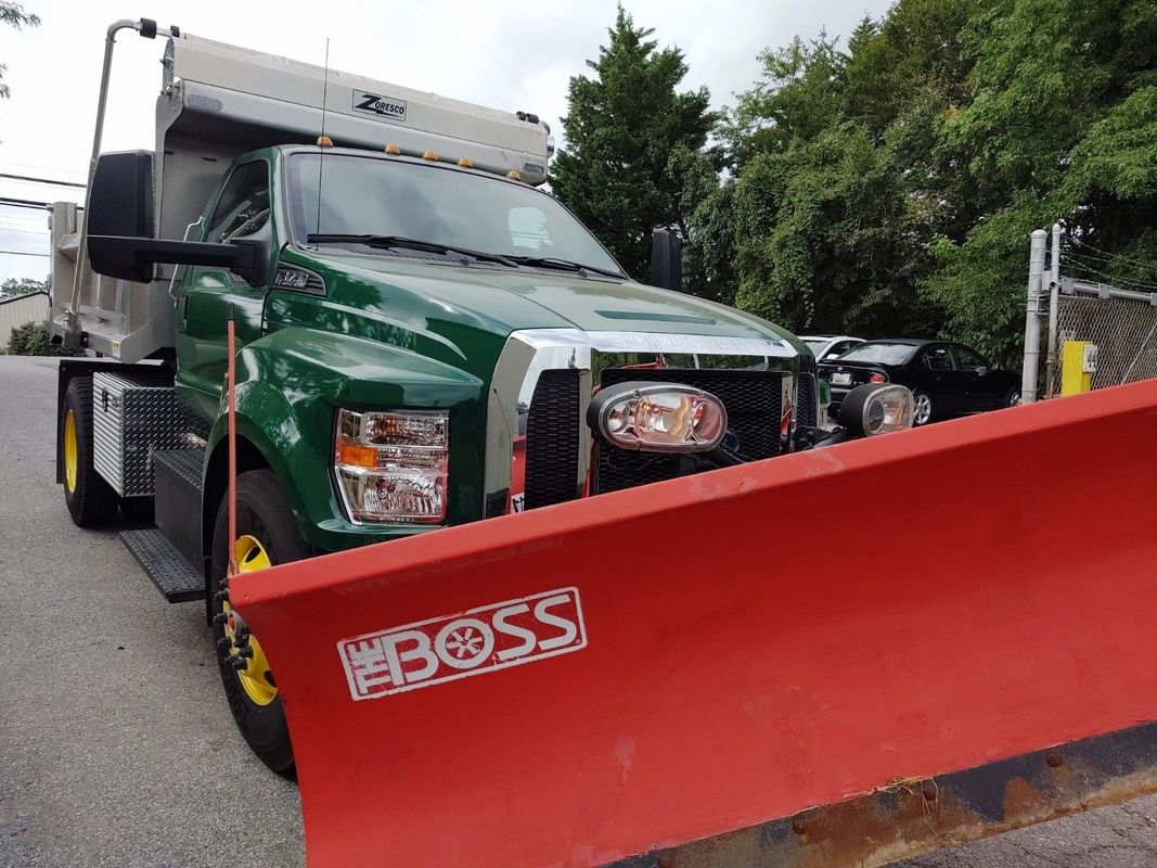 A green dump truck with a red plow attached to it.