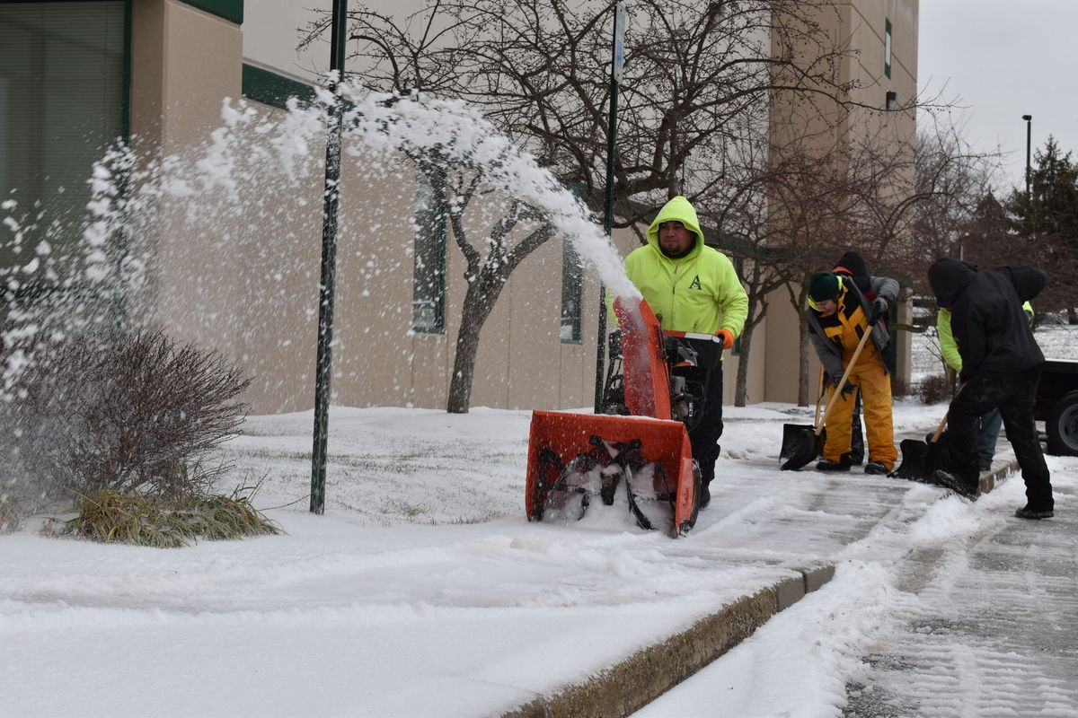 A group of people are clearing snow from a sidewalk with a snow blower.