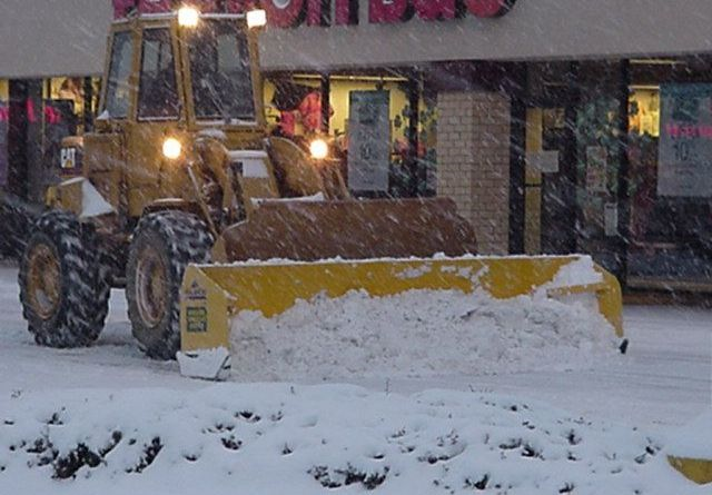A yellow tractor is clearing snow in front of a store