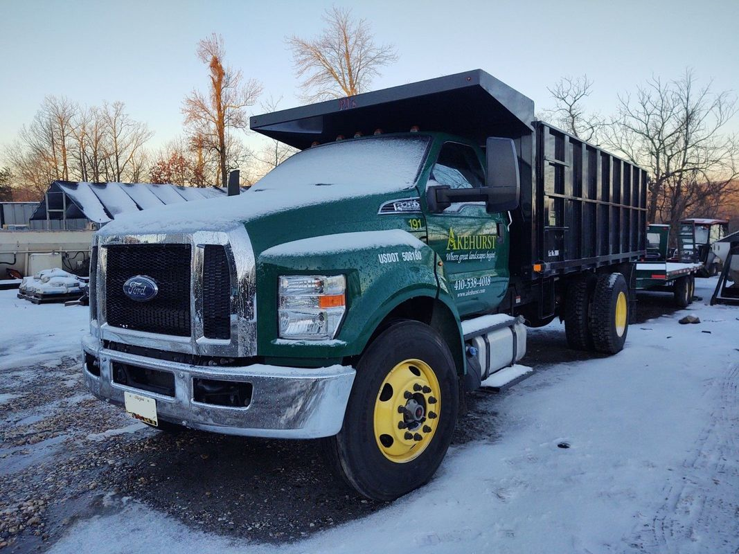 A green dump truck is parked in the snow.