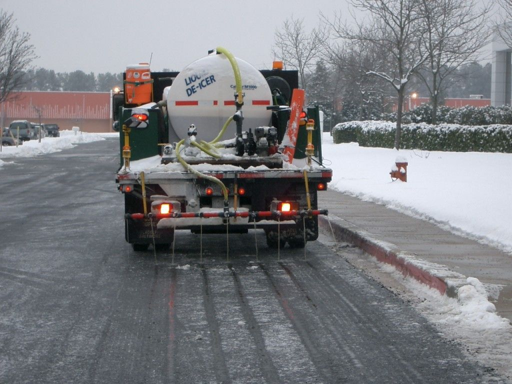 A truck is driving down a snowy street with a hose attached to it