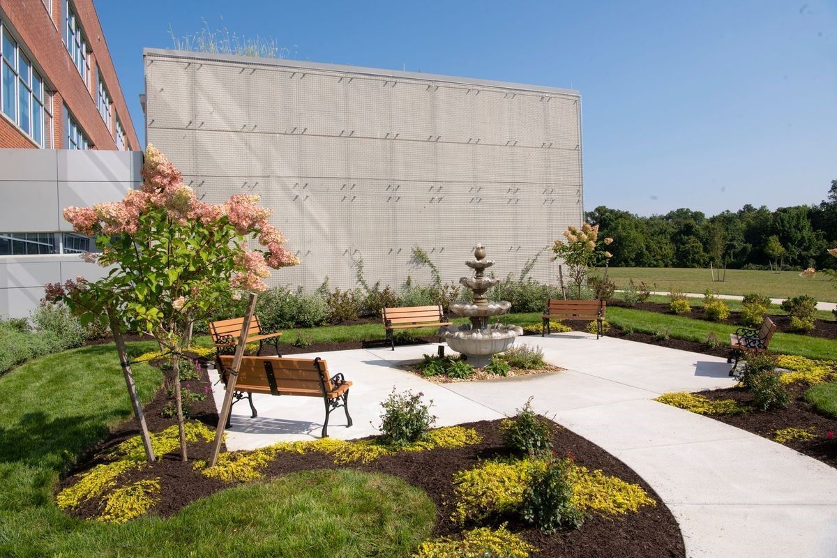 A park with a fountain and benches in front of a building.