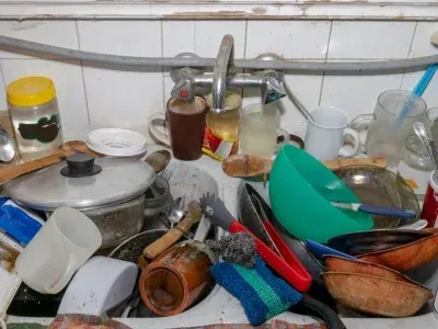 Un évier de cuisine en désordre débordant de vaisselle sale, de casseroles, de tasses et d'ustensiles.