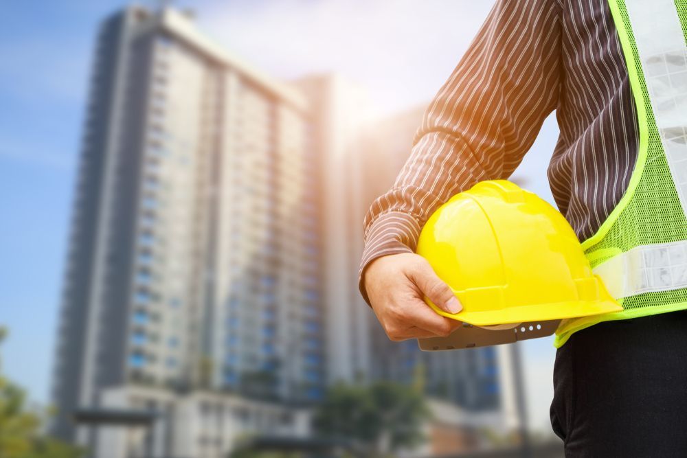 A Construction Worker is Holding a Yellow Hard Hat in Front of a Building — Search Partners in Melbourne, VIC