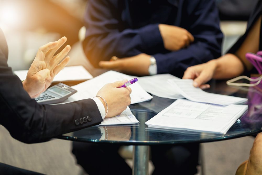 Business Meeting With Hands Pointing, Documents, and Calculator on a Glass Table — Search Partners in Melbourne, VIC