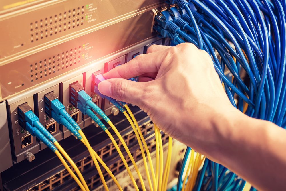 Hand Plugging a Network Cable Into a Server With Many Blue and Yellow Cables — Search Partners in Melbourne, VIC