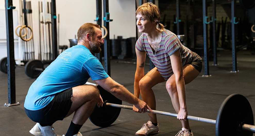 A woman doing a barbell deadlift with a trainer's guidance in a gym in Asheville, NC