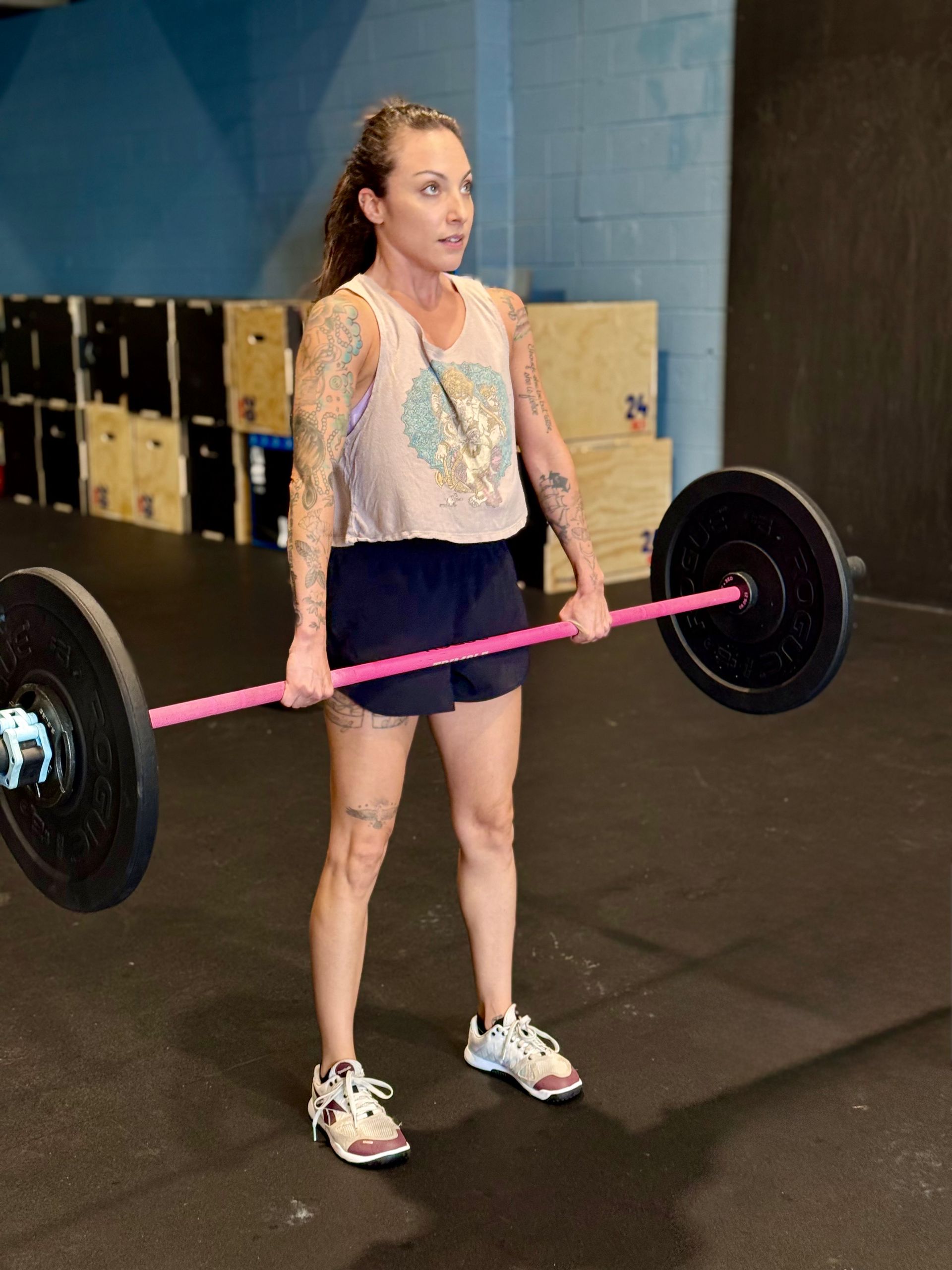Woman with tattoos lifting a pink barbell in a CrossFit gym in Asheville, NC