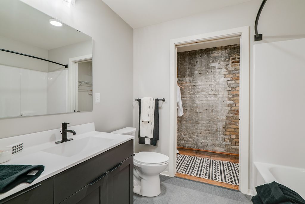 Modern bathroom with exposed brick shower, dark vanity, and black accents at Commission House, offers apartments in Lowertown St Paul, MN.