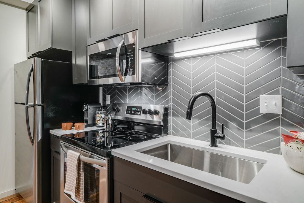 Modern kitchen with gray cabinets, stainless steel appliances, and herringbone tile backsplash.