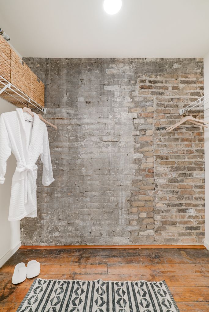 Walk-in closet with weathered brick and concrete wall, robe, baskets, and rug on a wood floor at Commission House, offers apartments in St. Paul, MN.