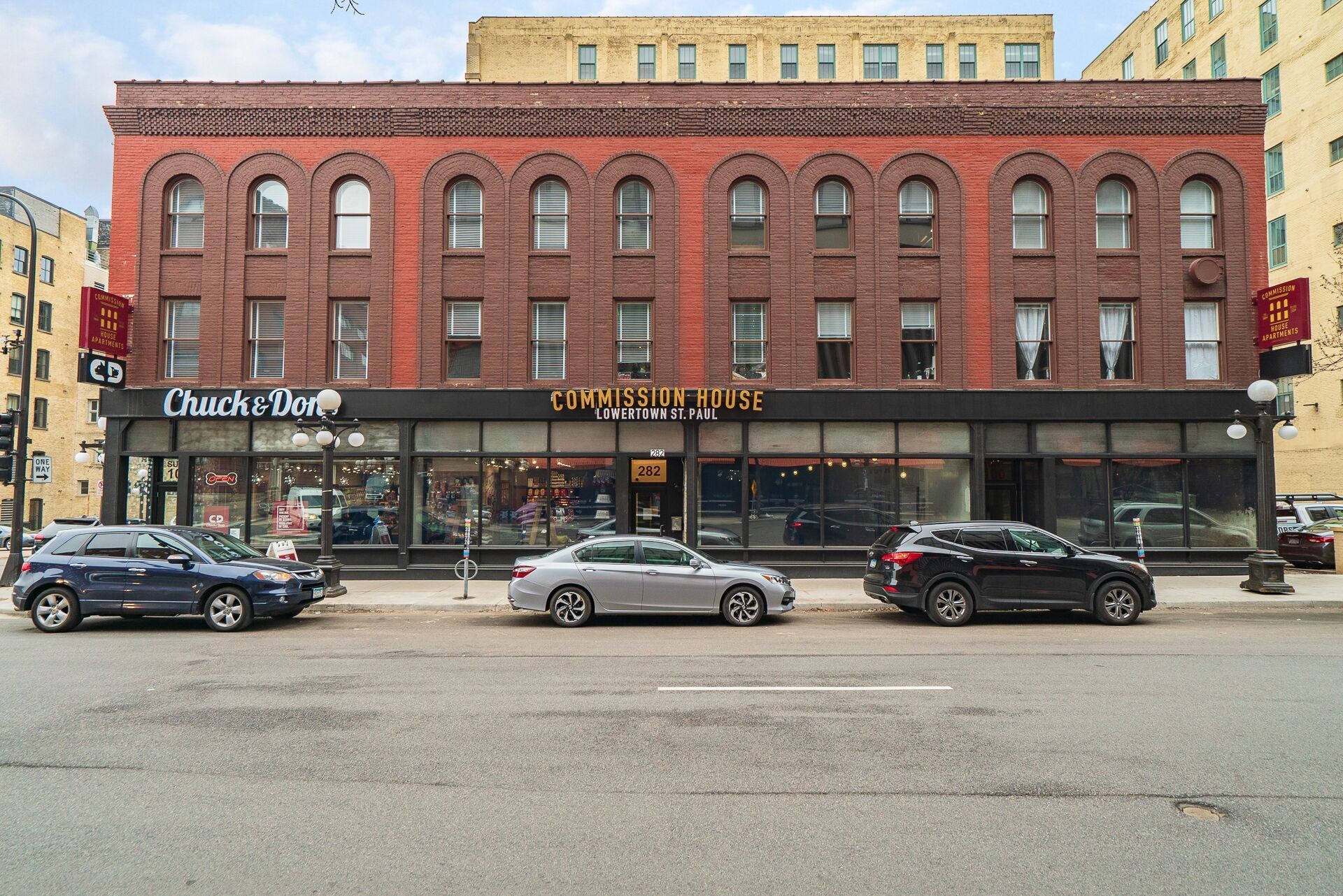 Red brick building with storefronts and parked cars on a city street at Commission House, offers apartments for rent in St. Paul's Lowertown neighborhood.