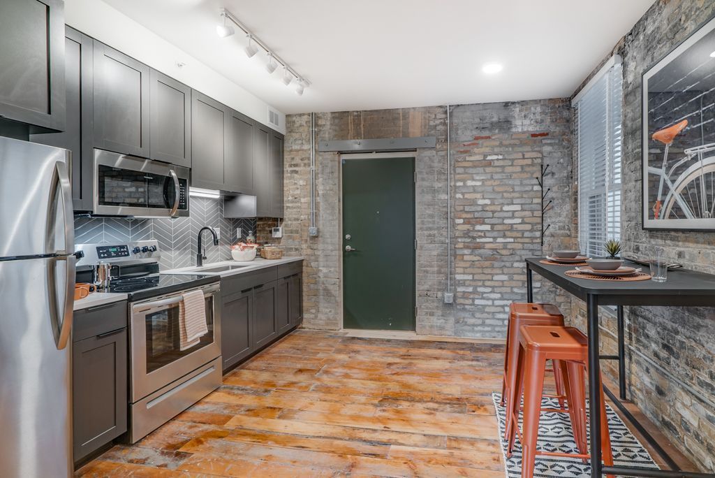 Modern kitchen with stainless steel appliances, dark gray cabinets, and exposed brick walls.