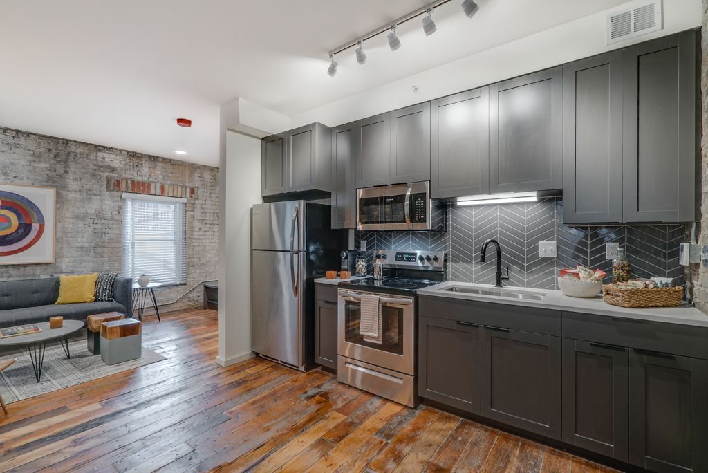 Modern kitchen with dark gray cabinets, stainless steel appliances, and exposed brick wall at Commission House, offers apartments for rent in St. Paul, MN.
