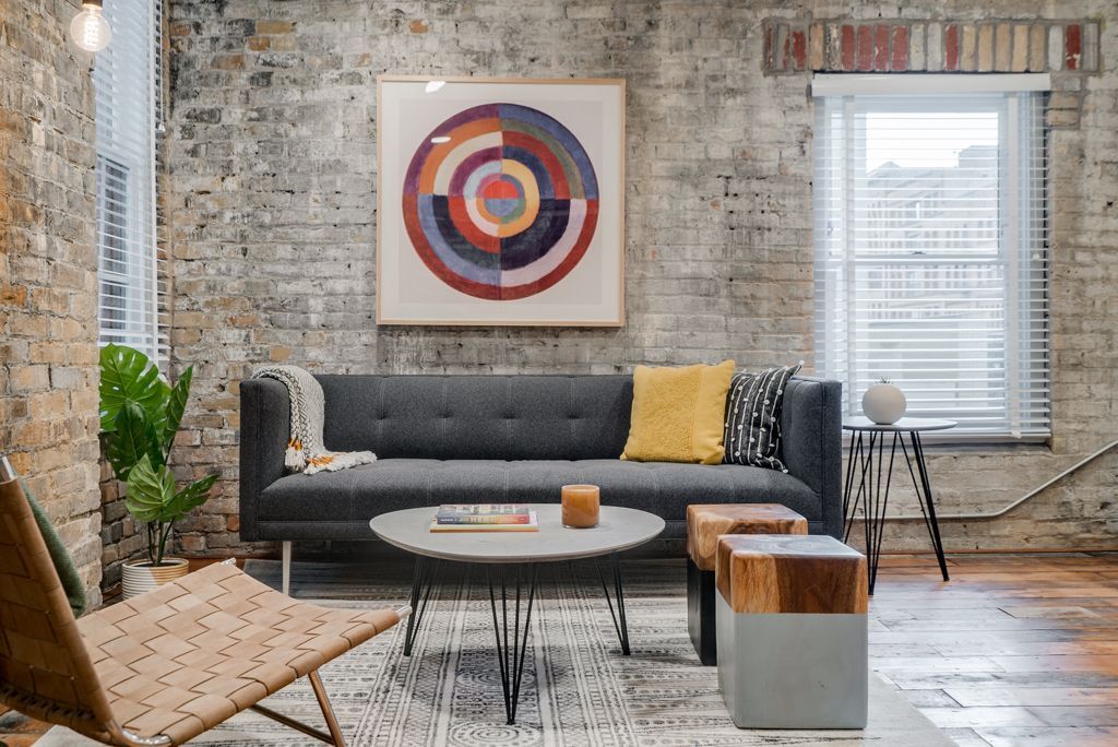 Living room with gray sofa, brick wall, abstract art, and round coffee table at Commission House, offers apartments in St. Paul, MN.