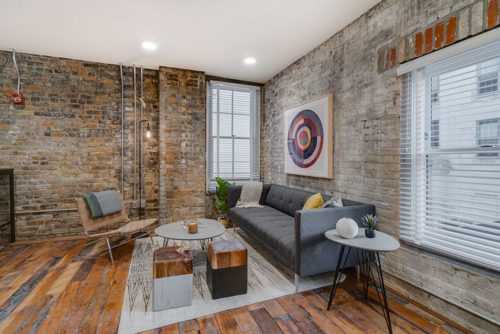 Living room with exposed brick walls, wooden floor, gray sofa, and modern furniture at Commission House, offers apartments in St. Paul, MN.