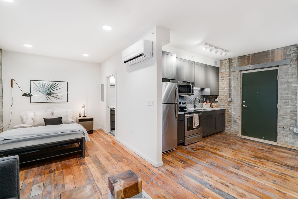 Studio apartment with open layout, wood floors, and modern kitchen at Commission House, offers apartments for rent in St. Paul, MN. Bedroom area visible.