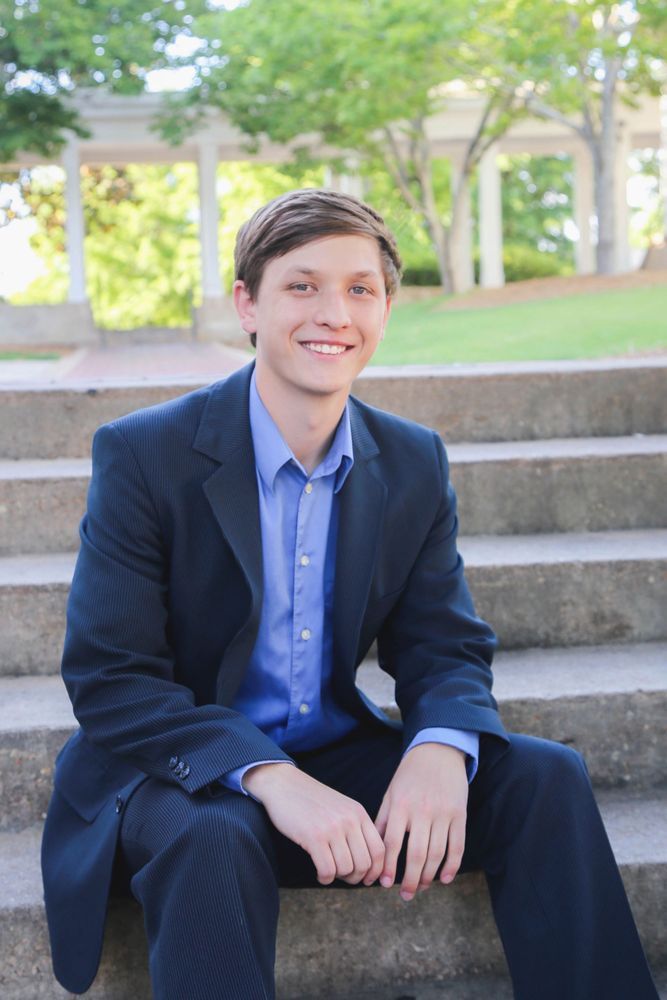 Man in blue shirt and blazer smiling while sitting on outdoor steps.
