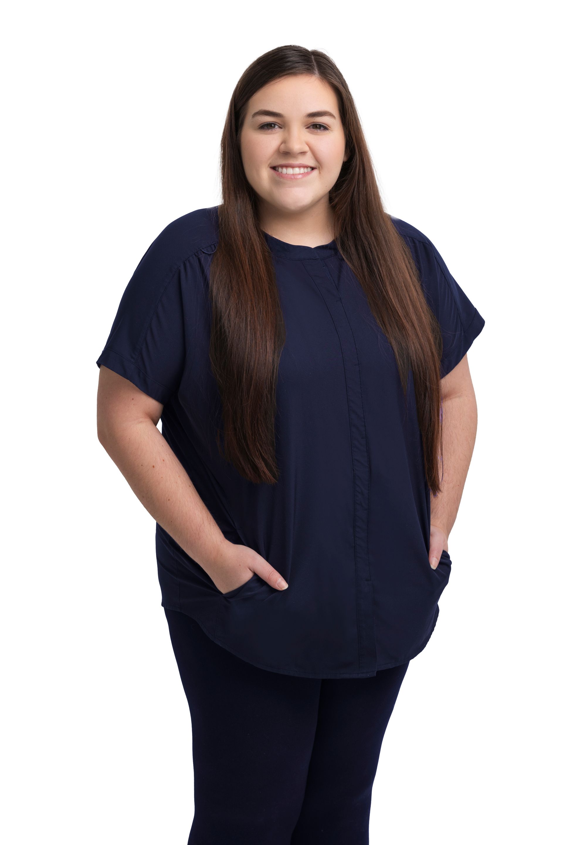 Smiling woman in navy shirt and pants standing against a white background, hands in pockets