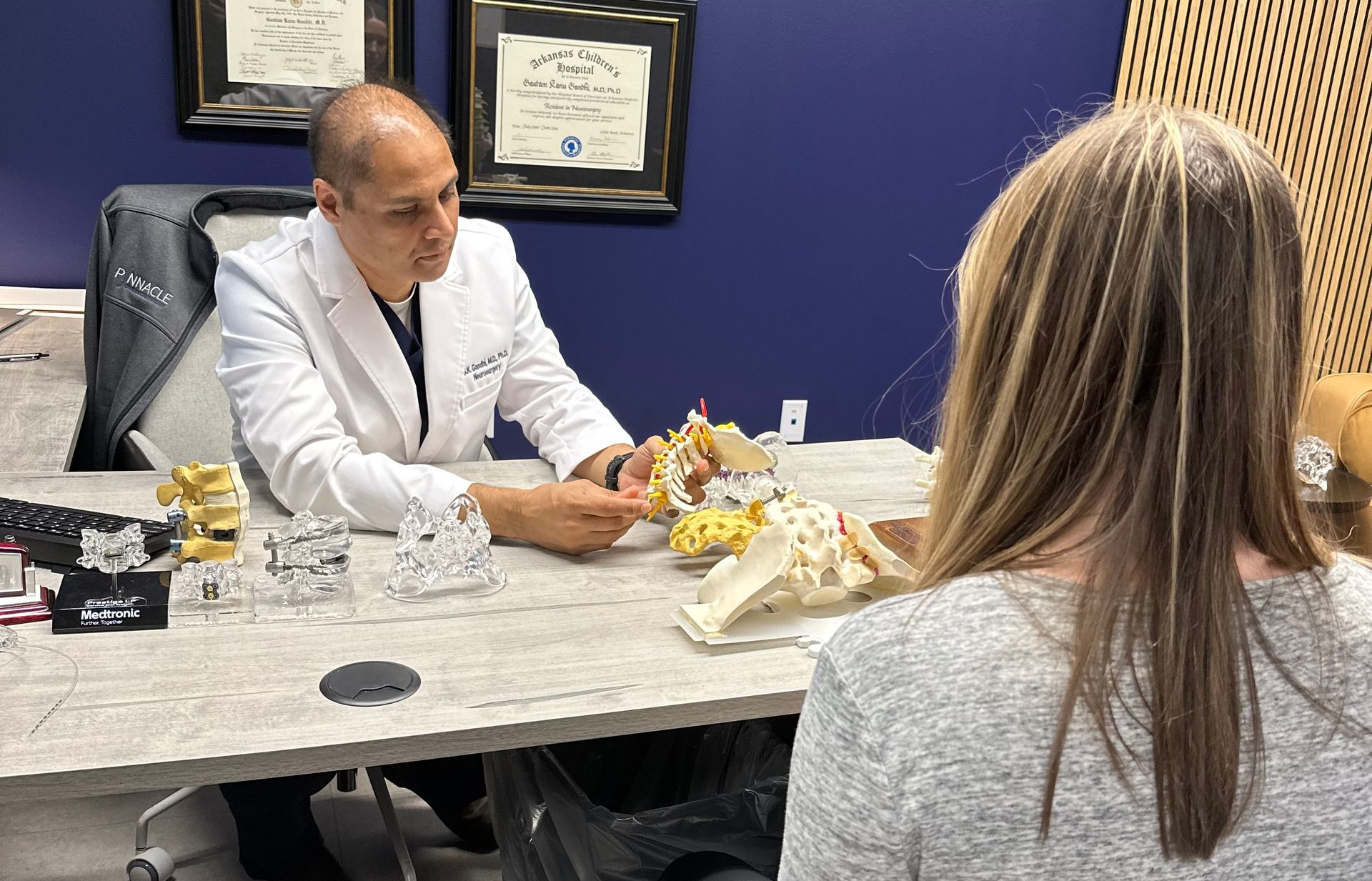 A photo of Dr. Gandhi consulting with a patient, using spine models to explain.