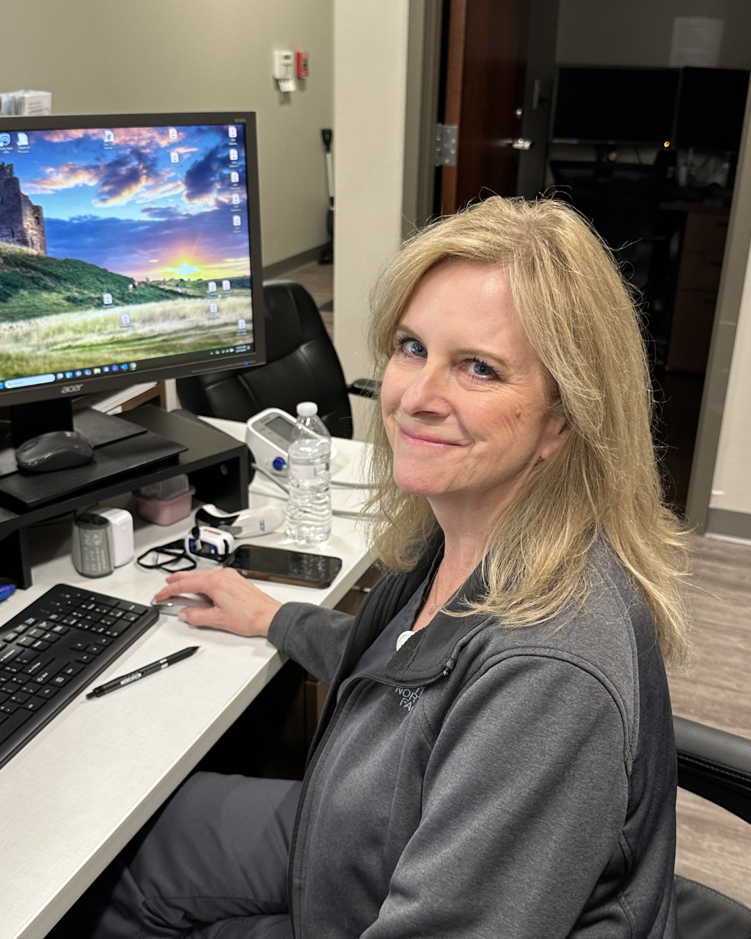 Woman seated at an office desk, smiling at a computer in a workspace.
