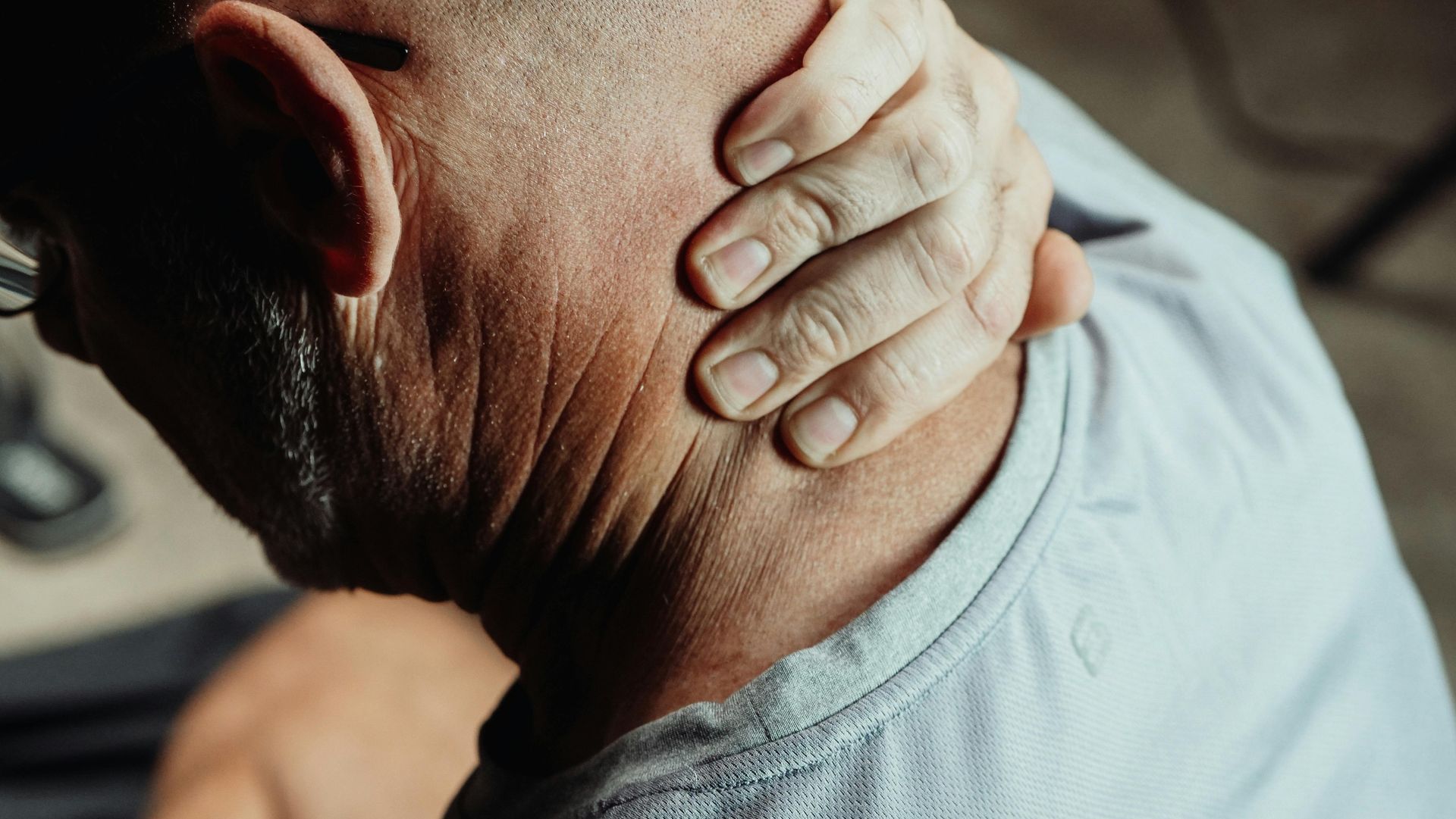 Hand holding the back of a person’s neck in a close-up, suggesting neck pain or tension.