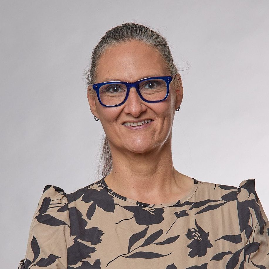 Woman with glasses and a floral print shirt smiling at the camera.
