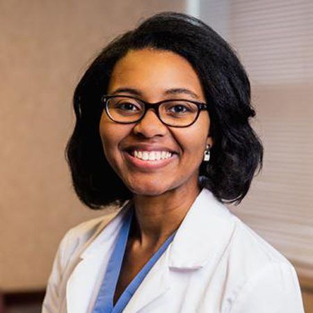 Smiling Black woman wearing glasses and a white lab coat.