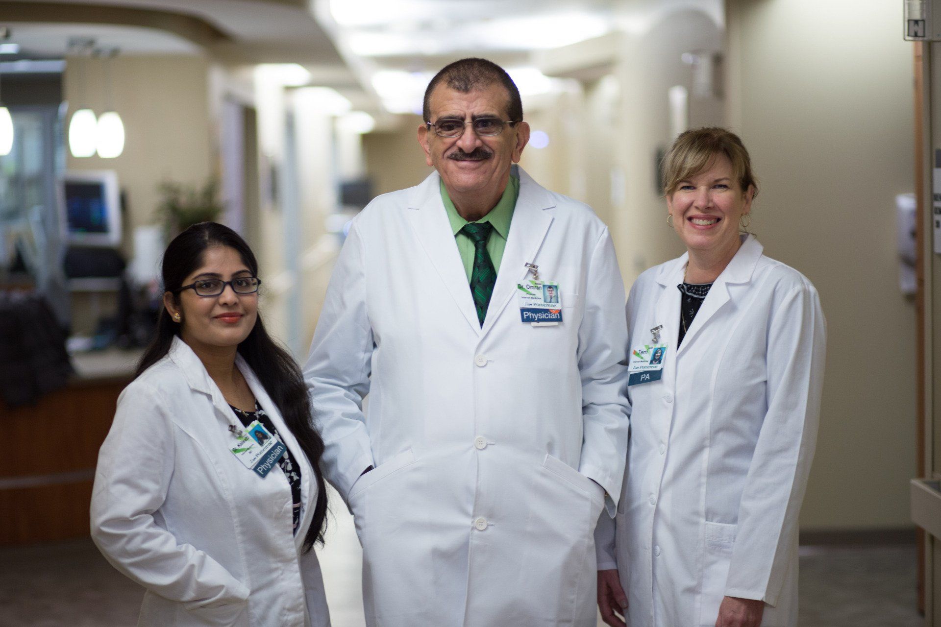 Three medical professionals in white coats stand in a hospital hallway.