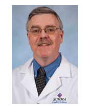 A man in a white lab coat with a blue shirt and patterned tie, wearing glasses, with a mustache.