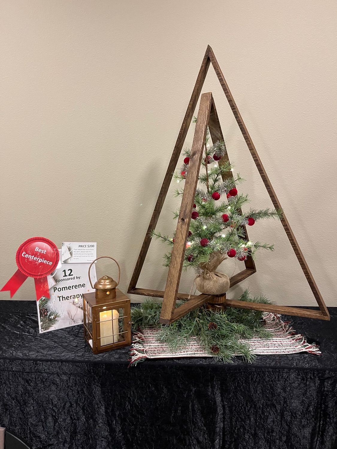 Christmas display with a small tree, lantern, and presents on a black tablecloth.