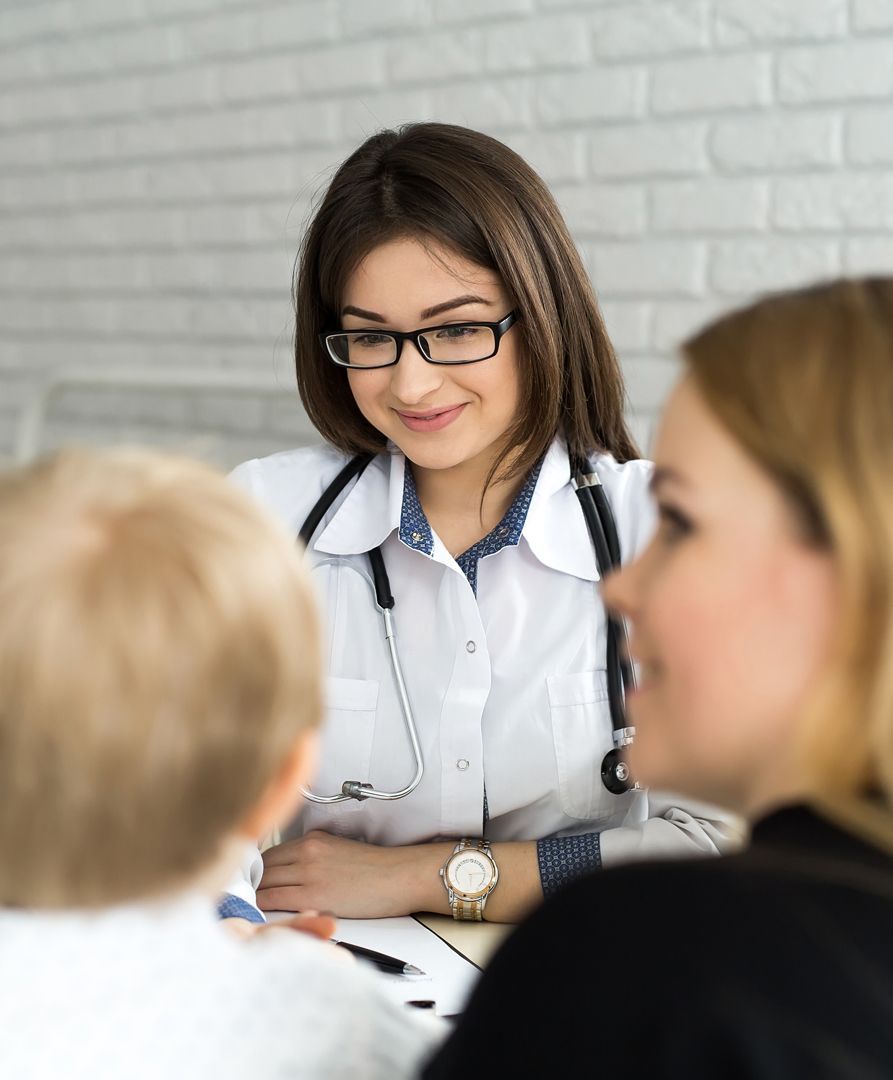 A doctor smiles at a patient in an exam room. The doctor, wearing glasses and a stethoscope.