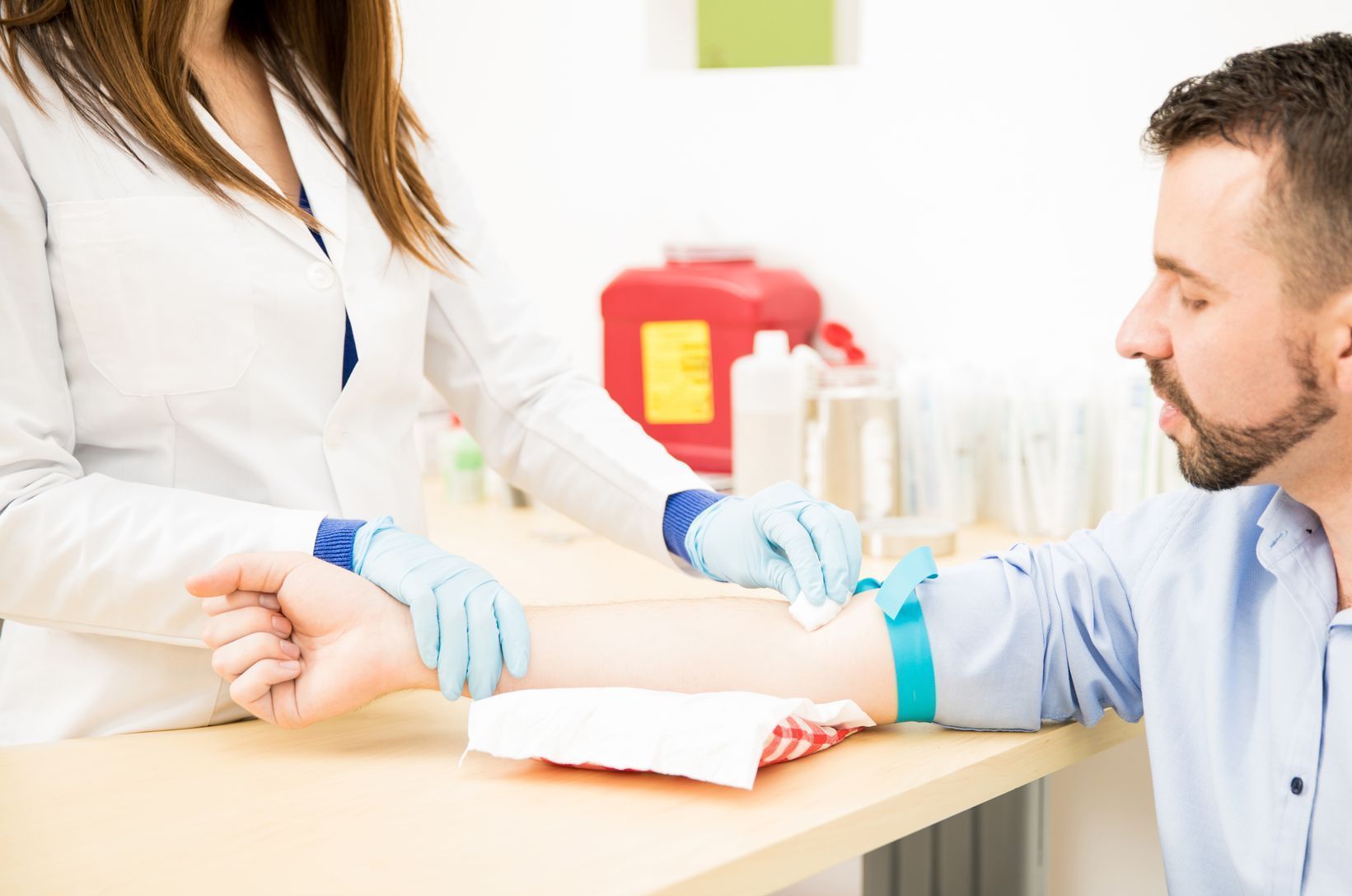 Nurse drawing blood from a man's arm. The nurse wears a white coat and gloves. A tourniquet is on the man's arm.