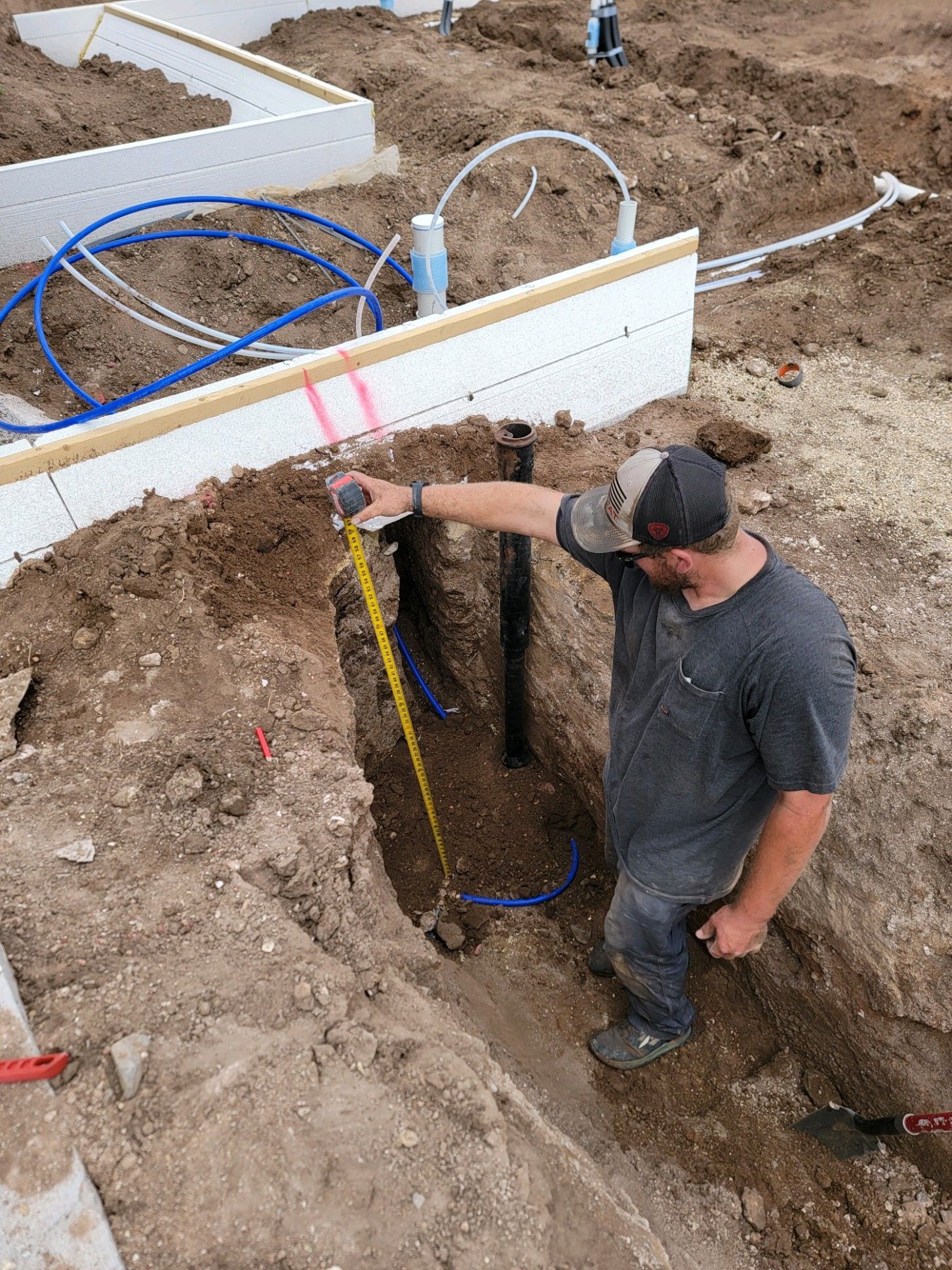 A man is measuring a hole in the ground with a tape measure.
